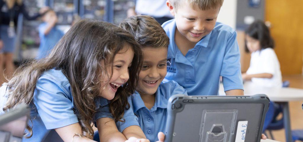 three lower school students looking at an ipad, private school